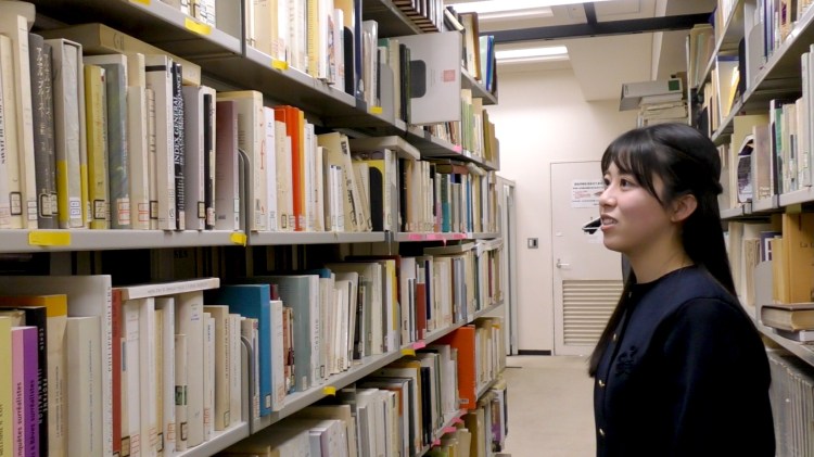 フランス文学専攻院生室_書架の説明をする山下さん